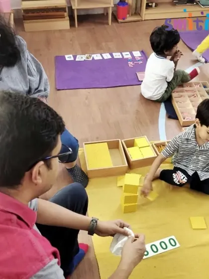 A father watches his son explore the golden beads, a Montessori material that makes the decimal system concrete. These moments of quiet observation build a strong connection between home and school.