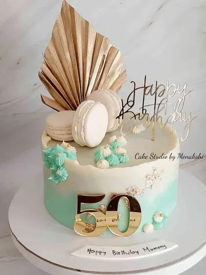 A beautiful 50th birthday cake for a mummy, made without fondant. The soft teal ombre is decorated with macarons, a golden palm spear, and a custom topper.
