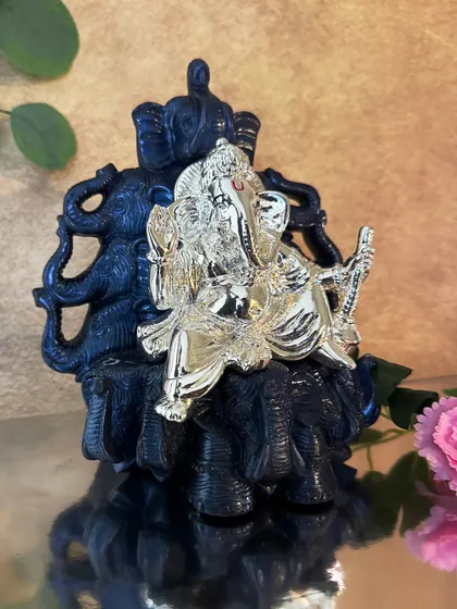 This silver-plated Ganesha idol sits upon a dark, intricately carved elephant throne. The contrast between the radiant silver and the dark base makes this a visually striking piece of devotional art.