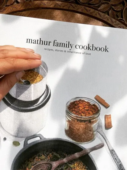 The cover of the Mathur Family Cookbook, featuring a stunning illustration of spices and cooking tools, representing the heart of their kitchen.