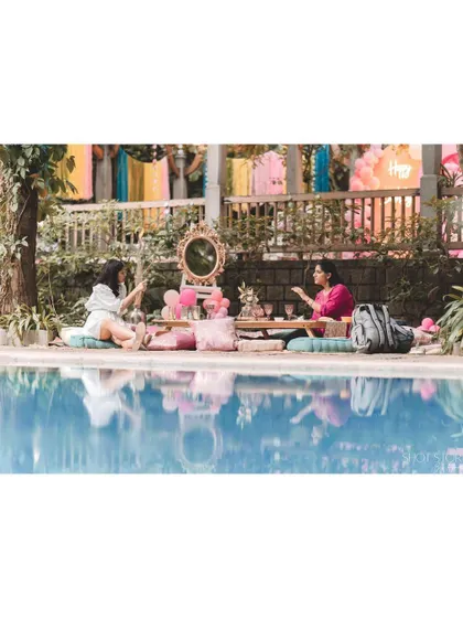 A serene poolside picnic setup. Two guests enjoy an intimate celebration with a low table and cushions, reflecting by the water.