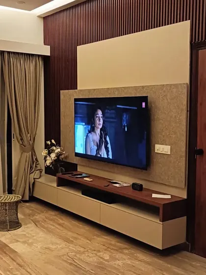 A close-up of a custom TV unit in a living room, featuring a beige console and a textured wall panel. This design is simple, elegant, and provides ample storage.