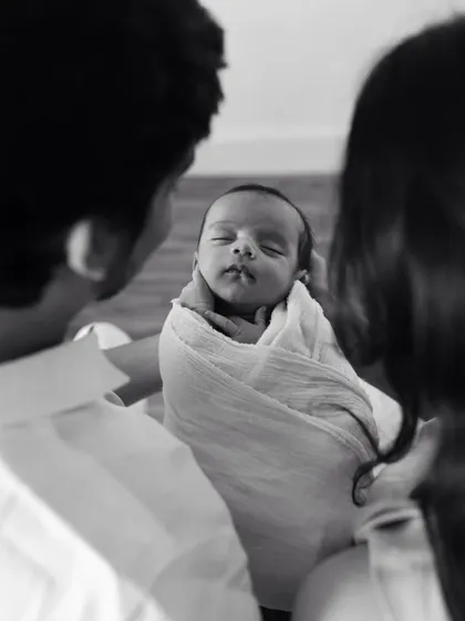 A black and white photo of parents looking down at their swaddled newborn. A beautiful, intimate moment.