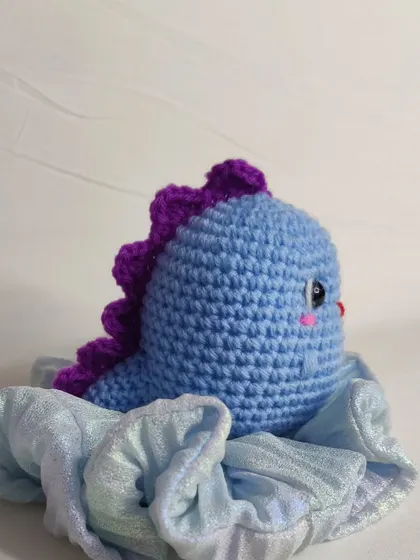 A blue dino keychain sitting on a scrunchie.
