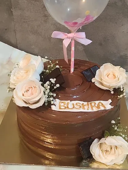 A delicious chocolate cake decorated with a balloon topper and fresh roses, combining celebration with indulgence.