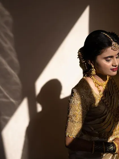 Playing with light and shadow to capture the bride's beautiful features. Her muhurtham makeup includes a warm, bronzed eyeshadow and a classic red lip, which looks stunning in this artistic shot.