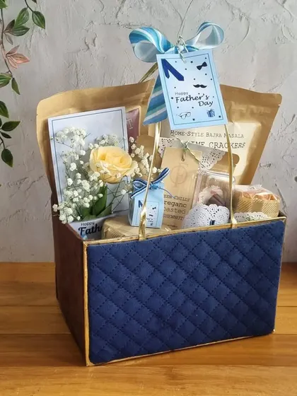 Celebrate Dad's big day with the perfect gift. This quilted blue box is filled with his favorite snacks and a fresh flower, showing him just how much he means to you.
