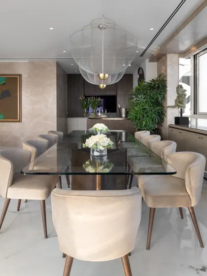 A head-on view of the dining table, anchored by the sculptural brass bases and surrounded by comfortable upholstered chairs. The large windows and light fixtures ensure the space is bright and inviting at any time of day.