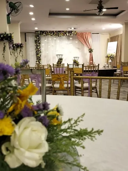 A detailed view of a table at an anniversary celebration, showing a floral centerpiece with white roses and yellow and purple accents, tying into the event's overall color scheme.