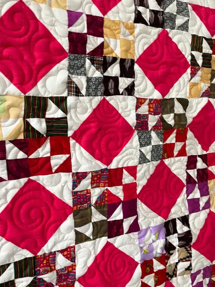 A close-up of a scrappy star quilt, showing the swirling quilting pattern stitched into the bright pink diamond blocks.