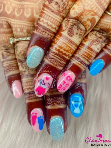 The cutest "Mom to Be" nails for a special celebration. We combined glittery blue and soft pink nails with custom hand-painted art, including baby clothes, footprints, and an hourglass, all set against the client's beautiful mehndi.