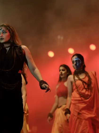A lead performer in a dramatic pose during a group performance. The red lighting and smoke create a powerful and theatrical mood.