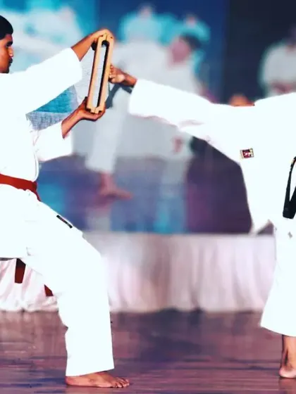 A student executes a precise side kick to break two boards held by a partner. This Tameshiwari drill develops accuracy, power, and trust between training partners.