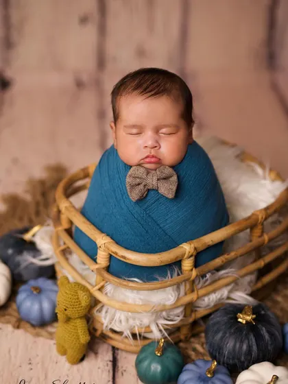 A similar setup showing the baby swaddled in a basket, this time with a simple bowtie. The focus remains on the baby's peaceful sleep.