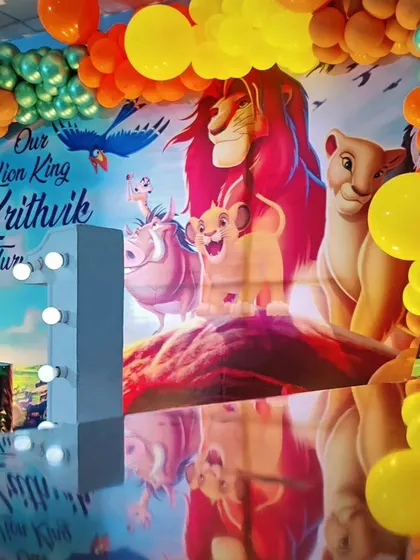 A majestic Lion King theme for a first birthday celebration. This setup features a large backdrop of Pride Rock, character-printed plinths, and a colorful balloon arch.