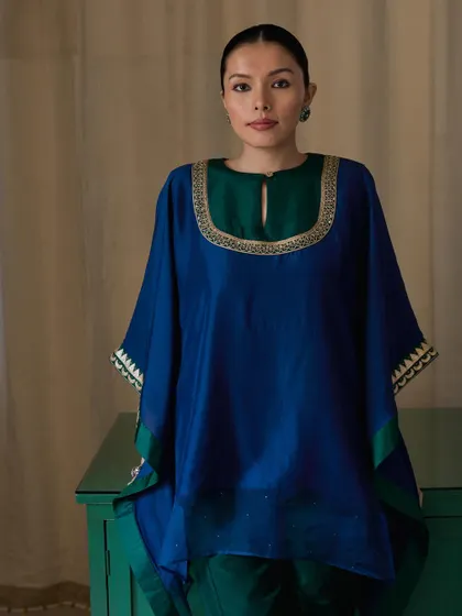 A studio portrait for a fusion fashion brand. The rich blue and green tones of the outfit are complemented by the simple, elegant posing and direct gaze.