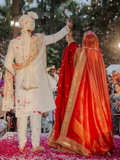 A beautiful back shot of the couple during the Varmala, showing the bride's stunning red lehenga and the celebratory petal toss.