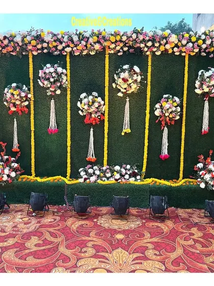 A creative photo wall with a green turf background and hanging floral arrangements. The design is fresh, modern, and perfect for guest photos.