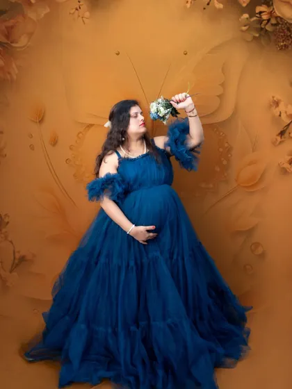 A mother-to-be in a flowing blue gown, holding a bouquet against a warm, butterfly-themed backdrop. A beautiful and artistic way to capture the pregnancy glow.