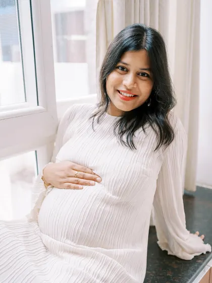 A lovely, bright portrait of the mother-to-be sitting by a window. Her direct, happy gaze at the camera radiates confidence and joy.