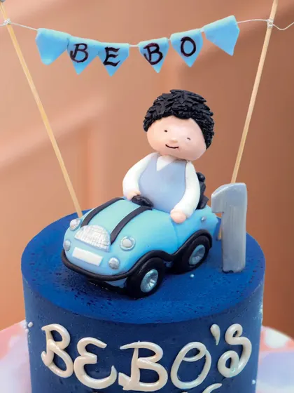 A close-up of the adorable topper for the car-themed cake, showing the detailed fondant work on the character and his little blue car.