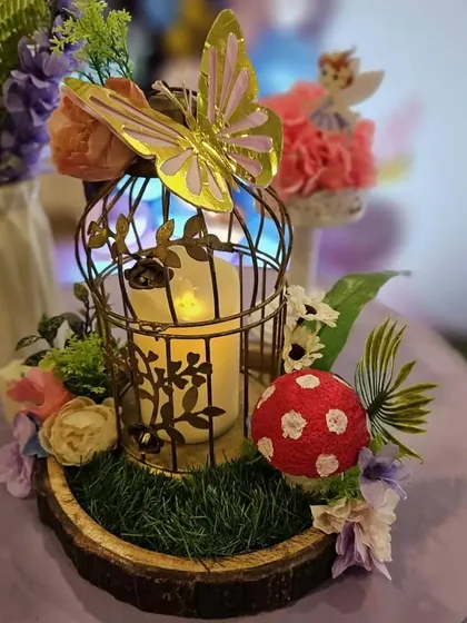 A whimsical table centerpiece featuring a birdcage with a candle, a mushroom, and a golden butterfly.