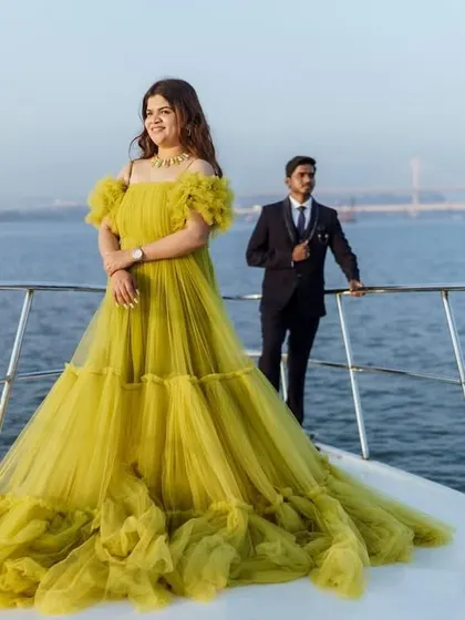 A stylish pose on the bow of a boat, featuring the tiered lime green ball gown. This image perfectly captures a modern and glamorous pre-wedding or maternity shoot.