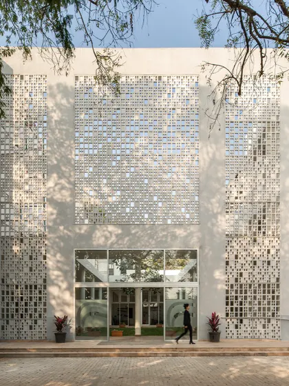The main entrance of Vidyashilp Academy is framed by large perforated screens. This design provides a grand sense of arrival while functionally serving to shade the glass entrance and ventilate the building's interiors.