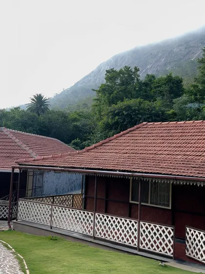 Our cottages at Nandi Hills offer a charming stay with their tiled roofs and classic design, set against a mountain backdrop.