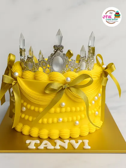 A cake fit for a queen. This vibrant yellow cake is decorated with classic buttercream piping, pearl details, and a stunning silver tiara, making any birthday feel like a royal event.