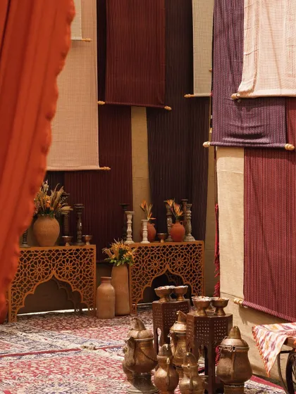 A cozy corner of the bazaar setup, featuring carved wooden tables, copper lanterns, and walls draped in earthy-toned fabrics.