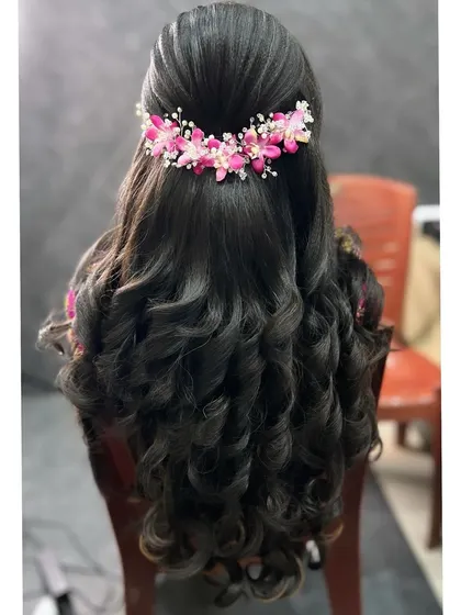 A classic half-updo with big, bouncy curls. I added a beautiful pink floral hairpiece to match the bride's reception saree, creating a cohesive and elegant look.