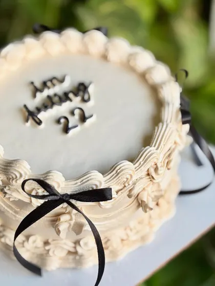 Dripping in old-world charm. A close-up of this vintage dream cake, with its off-white buttercream, intricate piping, and chic black ribbons.