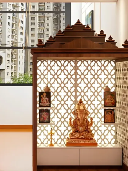 This pooja mandir, set against a window with a city view, is a perfect urban sanctuary. The traditional wooden structure with intricate jali work and a spacious cabinet below is both beautiful and functional.