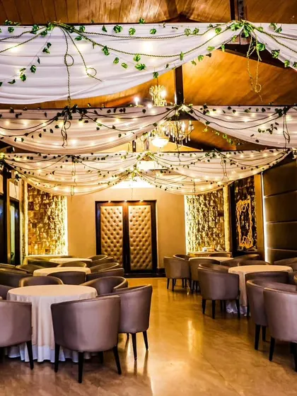 A rustic and elegant indoor venue decoration. We draped the ceiling with white fabric and intertwined fairy lights and green vines, creating a warm and magical ambiance for a dinner or reception.