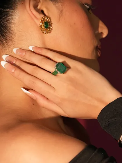 A close-up of a stunning emerald set. The large emerald-cut ring and matching oval earrings are set in gold with diamond accents, showcasing the deep, rich color of the stones.
