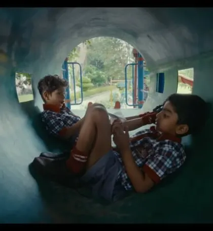 Two boys in their school uniforms, sharing a moment in a playground tunnel. The styling is simple and doesn't distract from the emotional core of the scene.