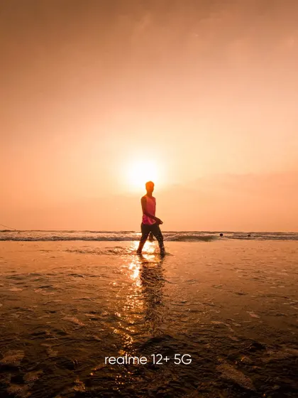 A silhouette of a person walking in the shallow water at sunset. The reflection on the wet sand and the powerful sun create a serene and contemplative image.