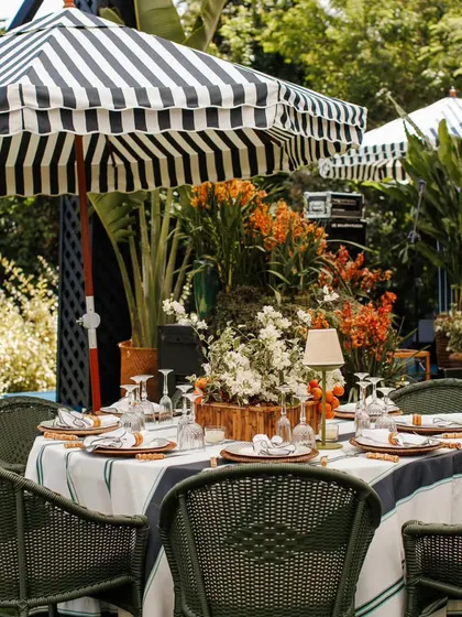 A beautifully set table under a striped patio umbrella. This setup from a garden party shows how I mix patterns and textures, from the wicker chairs to the custom tablecloth, for a layered look.