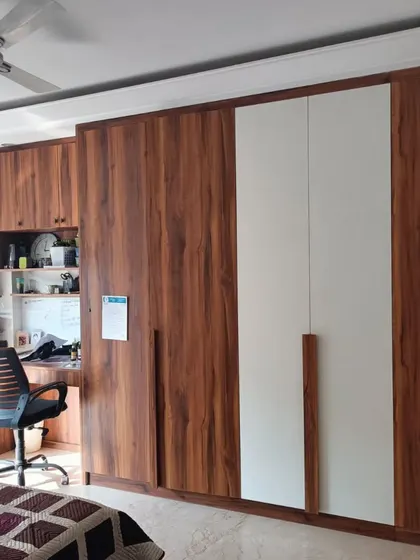 A custom-built wardrobe and study unit in a bedroom. The design combines white and wood-grain laminates, seamlessly integrating storage with a functional workspace.