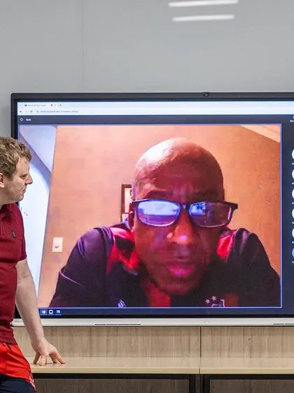 A speaker on a video call interacts with the in-person audience, facilitated by one of our trainers, showcasing the hybrid nature of our conferences.