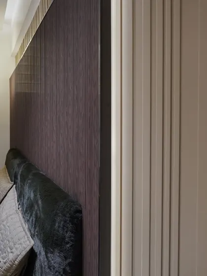 A detailed shot of a bedroom, focusing on the texture of the fluted wall panels and the velvet headboard.