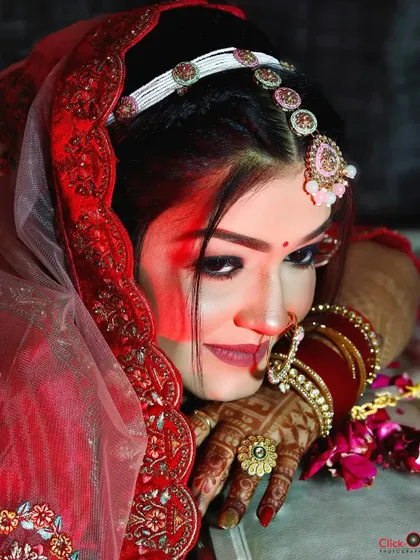 A close-up shot of a bride in her red wedding attire, highlighting her intricate makeup and jewelry with dramatic red lighting.