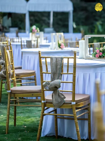 A close-up of a simple, elegant outdoor table setting. The white linens and rustic chair decor create a clean and sophisticated look for a daytime event.