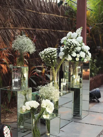 Mirrored pedestals with white floral arrangements add a touch of modern elegance to the rustic beach setting.