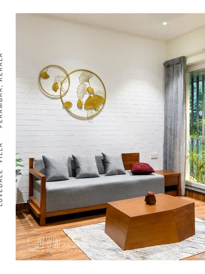 A cozy living area in Lovedale Villa, with a simple wooden sofa, geometric coffee table, and gold wall art against a white brick wall.