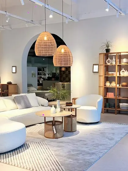 A wide view of a living room designed with the Siena collection. The curved Poet Sofa is perfectly complemented by the rattan and travertine of the Siena tables and bookshelves, creating a bright, airy, and cohesive tropical-inspired sanctuary.