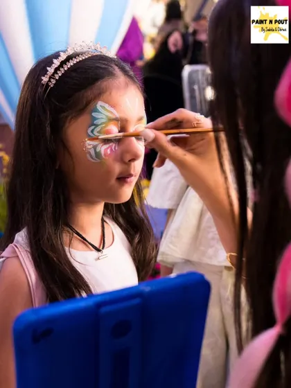 A young client getting a multi-colored butterfly design painted around her eyes. We take great care to be gentle and precise, especially with our youngest customers.
