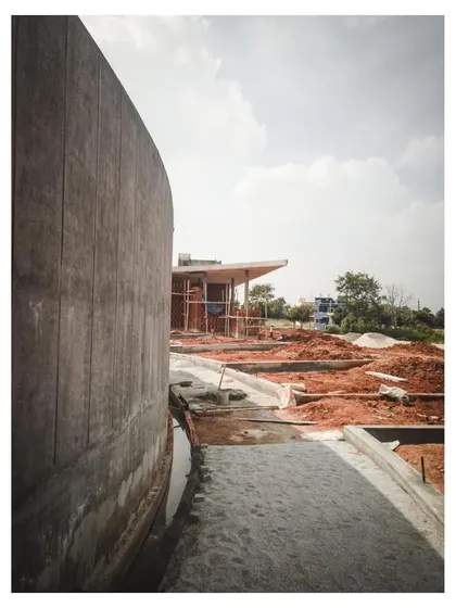 The exterior of the memorial's concrete gallery wall during the construction process. The image captures the texture of the concrete and the surrounding red earth, showing the project in its elemental state.