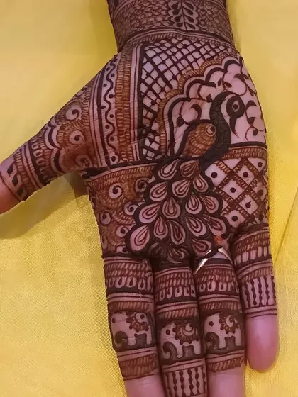 A detailed close-up of a peacock on the palm, with tiny elephants decorating the fingertips.